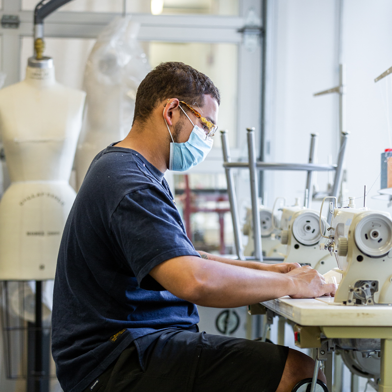 student working at sewing machine while wearing surgical mask during covid-19 pandemic