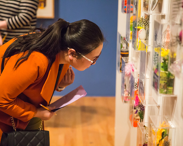 student with glasses and floral sweater examining artwork mounted to wall