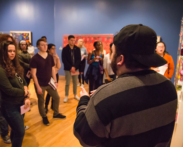 a large group of entrepreneurship and innovation students listen to a presenter on a field trip