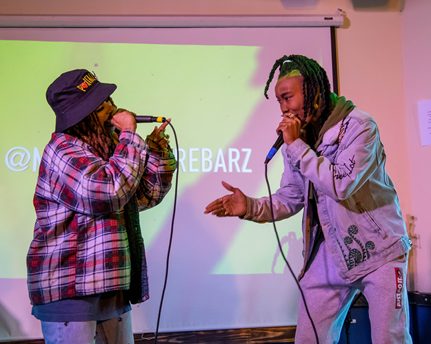 two masters in entrepreneurship for creatives rap into microphones on stage