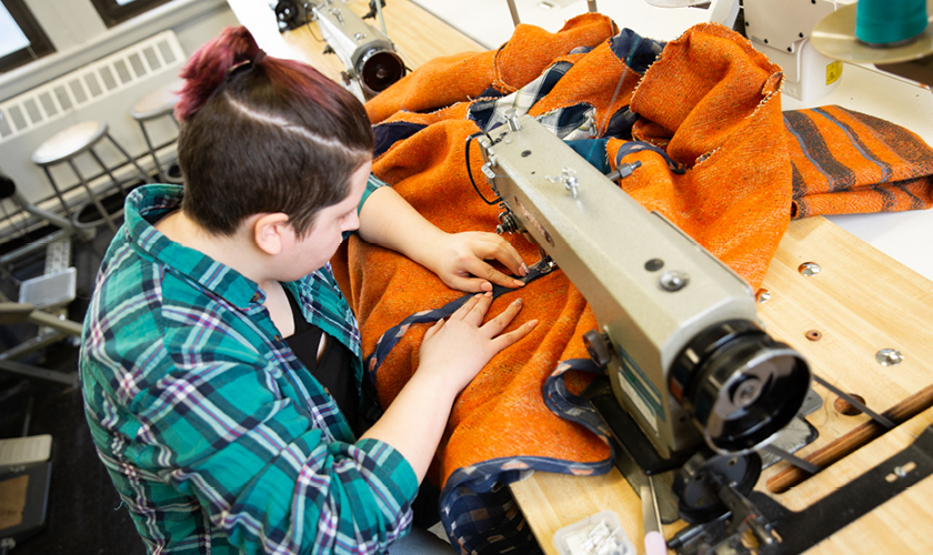 a fashion design major uses a sewing machine on orange fabric