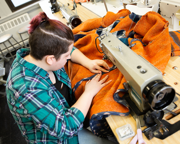 a fashion design major uses a sewing machine on orange fabric