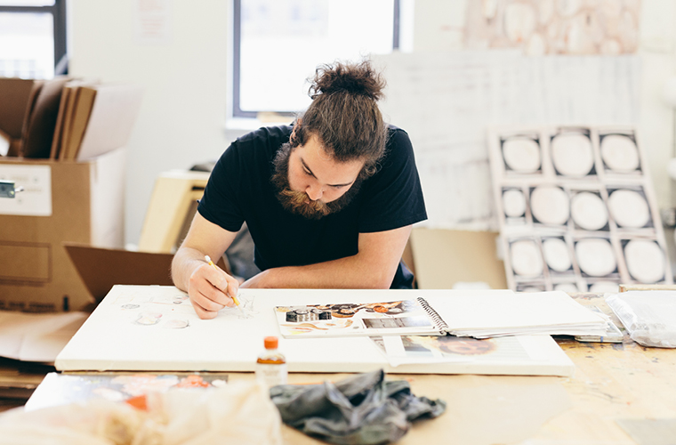 a master of fine art student leans over a table working on an art piece