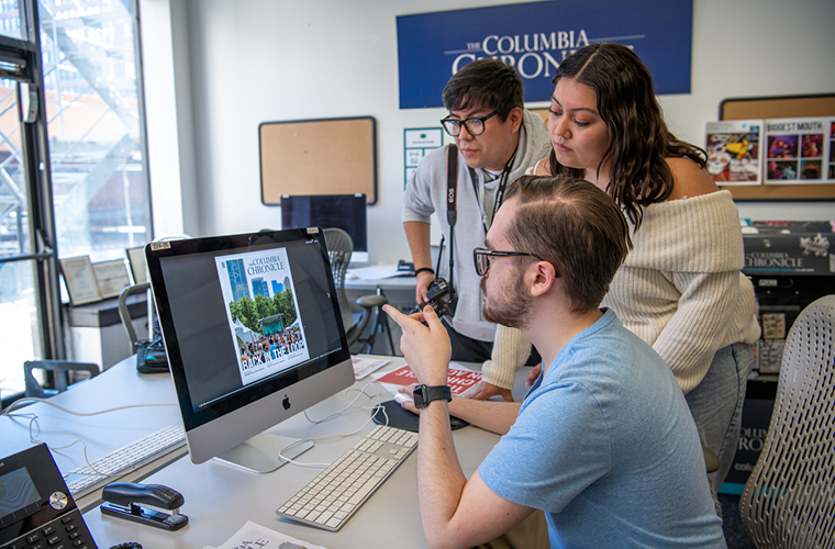 Journalism students working together around a computer screen