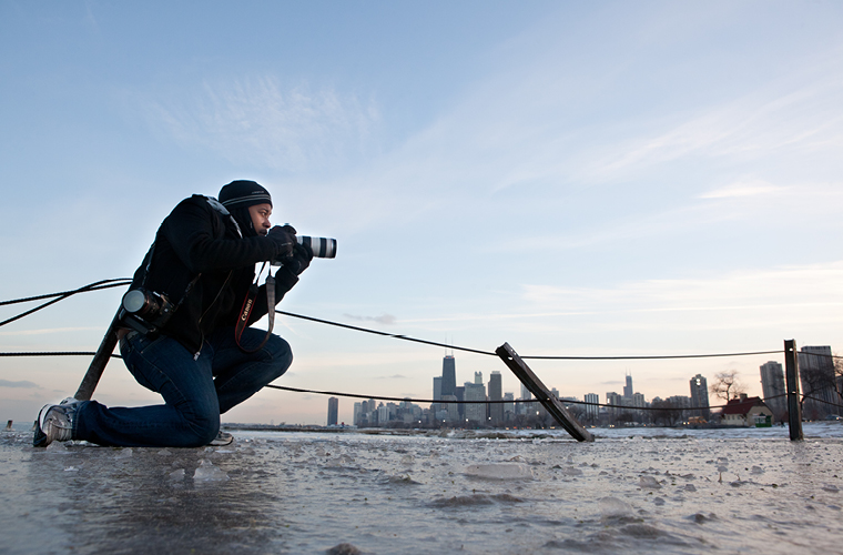 a student kneels outside next to lake michigan taking pictures in the winter