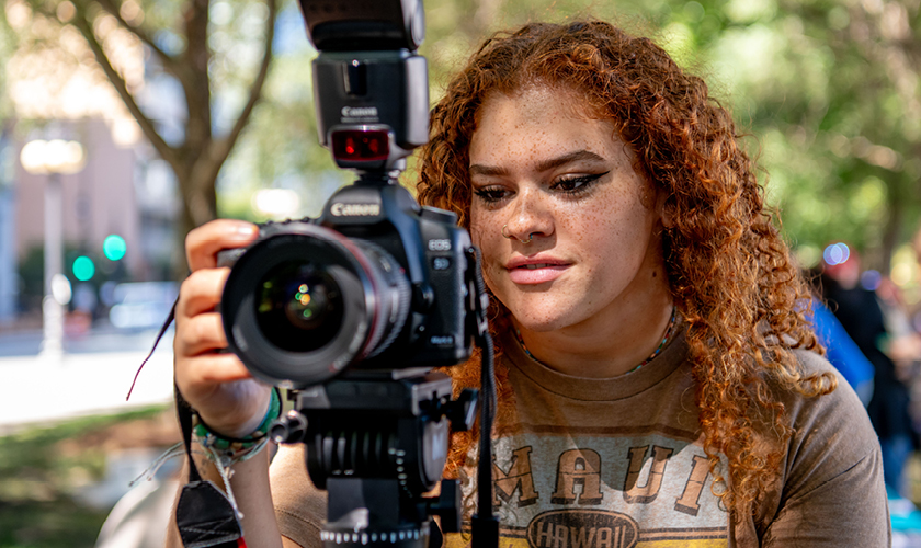 a photojournalism major uses a dslr camera to photograph an outdoor event