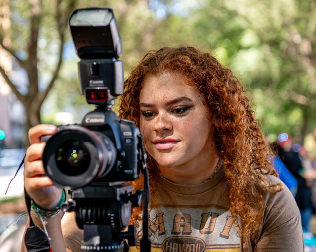 a photojournalism major uses a dslr camera to photograph an outdoor event