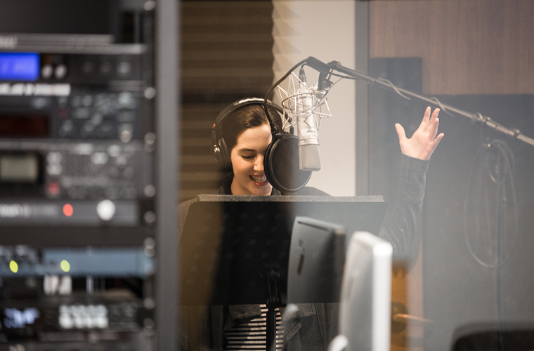 a radio student records their voice in front of a microphone in a sound booth