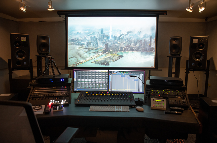 a large screen and lab filled with sound design equipment