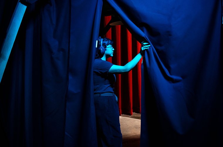 student wearing headphones working on stage holding curtain