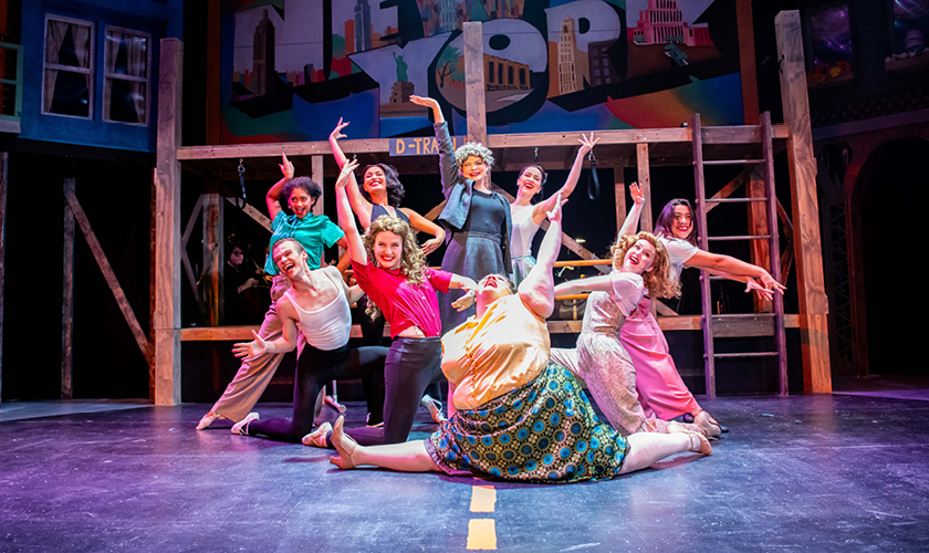 a large group of theatre majors perform on stage in colorful costumes