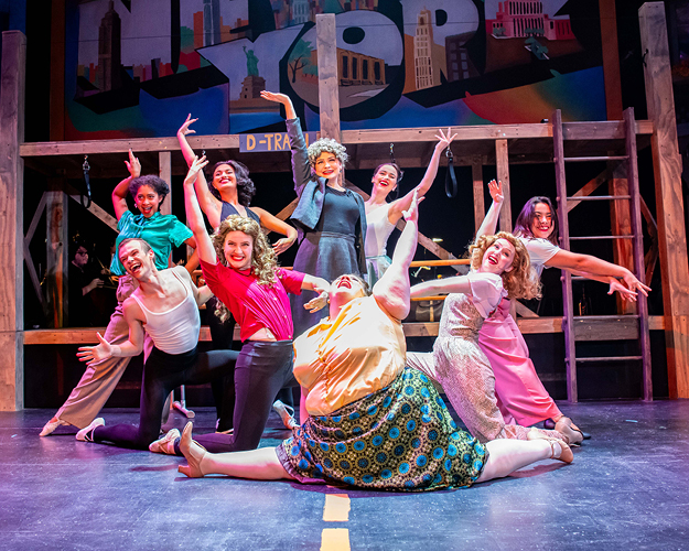 a large group of theatre majors perform on stage in colorful costumes