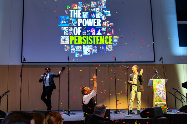 Two students on stage at Gala Fundraiser and a student in the audience throwing confetti