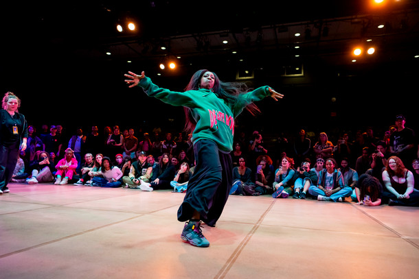 A Columbia student dances with their arms wide to the sides during a hip hop demonstration. A large crowd watches from behind. 