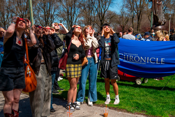 A group of students stand in Grant Park in front of a Columbia Chronicle banner to watch the solar eclipse in April 2024.