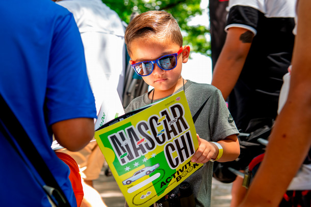 A little boy with sun glasses looks over a NASCAR activity book made by Columbia students