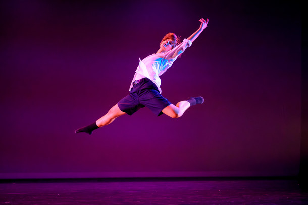 A dancer leaps in the air on stage bathed in purple light. 