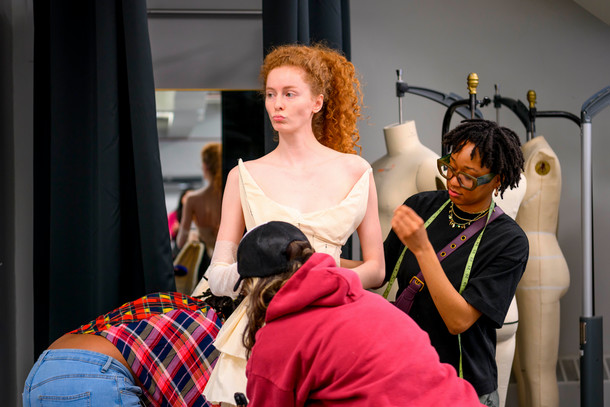 a model stands surrounded by three designers who work on a wedding dress design