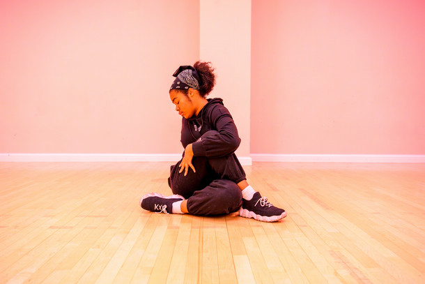 A Columbia student poses on the floor during a dance class. The room is bathed in pink light.