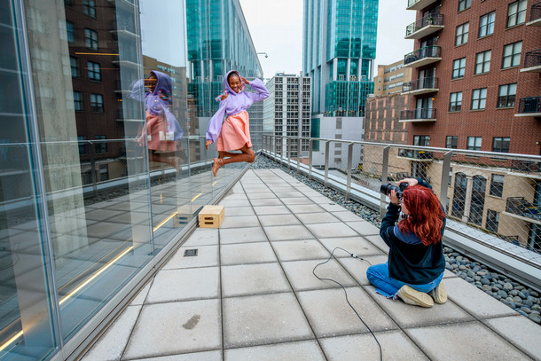 On a Student Center balcony a photography student captures a fashion student jumping off a block for a modeling photo.