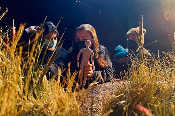 three people working on stop-motion set with human-like figure in grassy environment