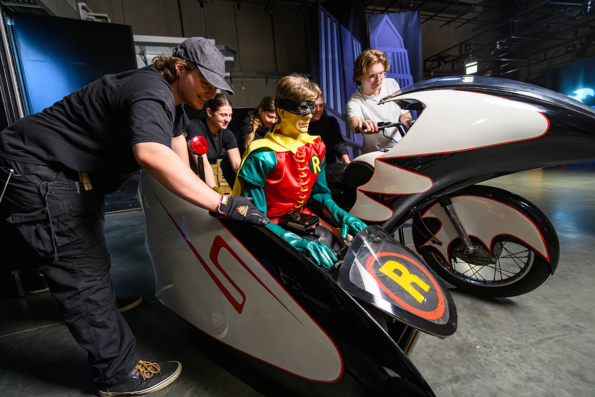 students pushing bat motorcycle with robin character inside